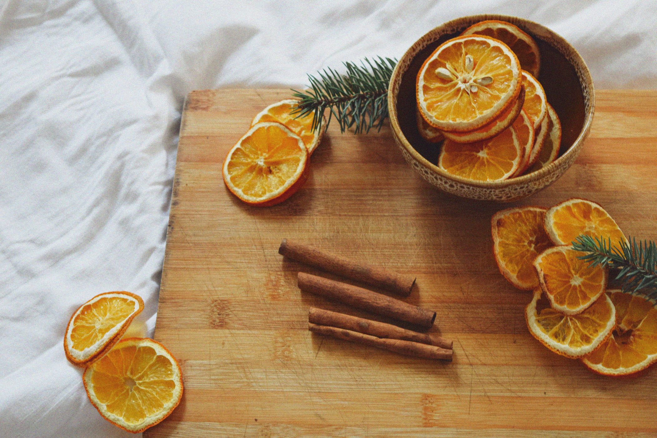 Dried oranges cut up on a wooden dish with cinnamon sticks.