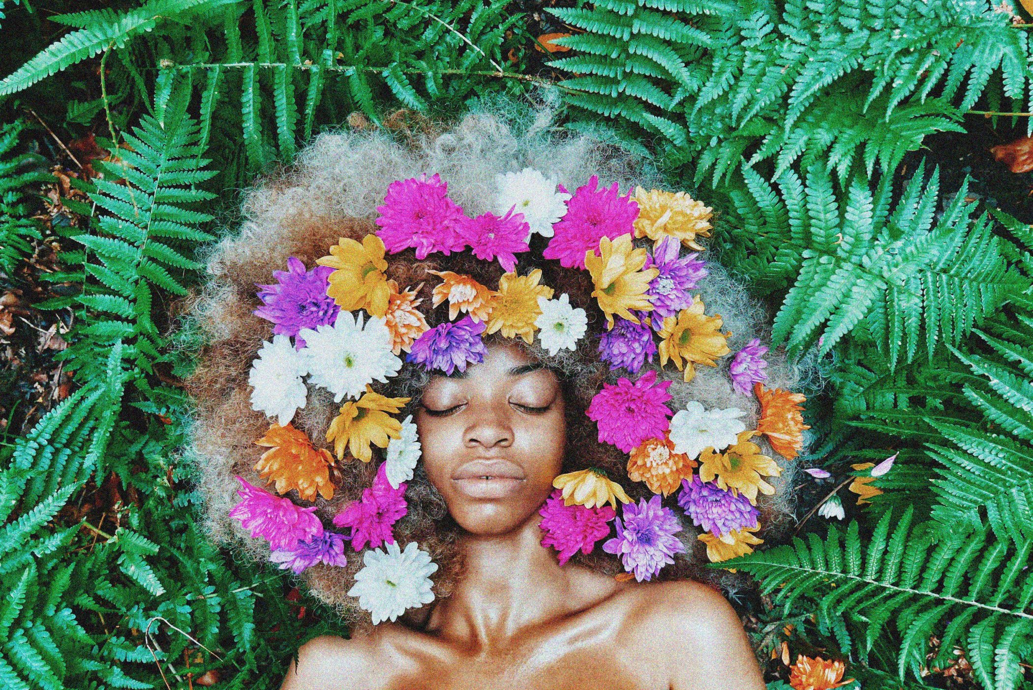 Woman laying down in green leaves with flowers in her hair.