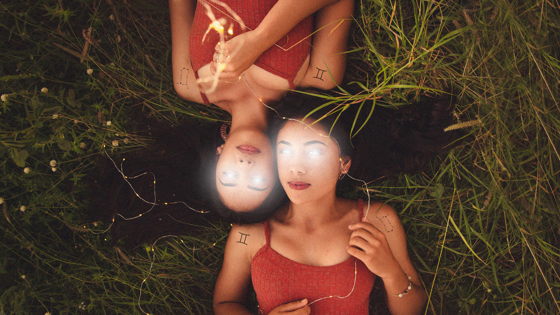 Twins laying down in grass with light beams coming from their eyes and Gemini tattoos.